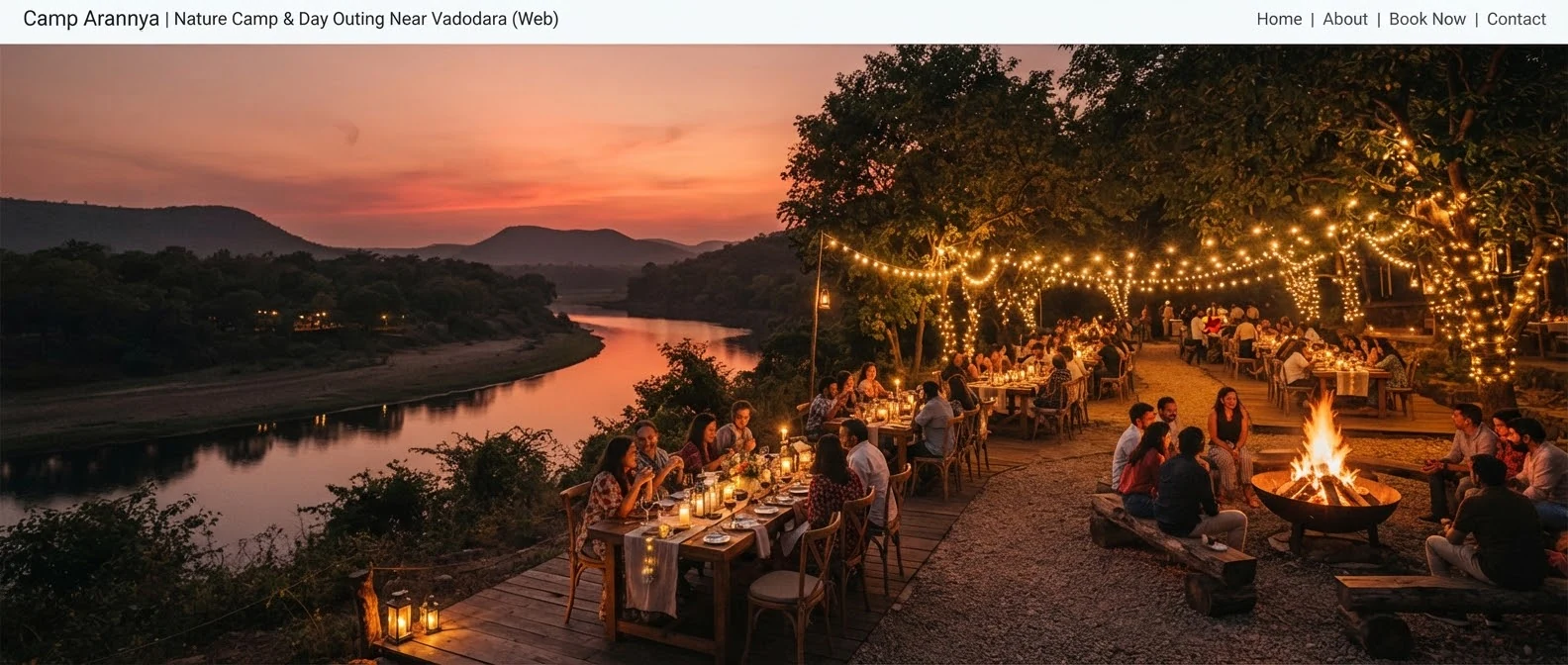 Panoramic twilight dinner scene at Camp Arannya overlooking a tranquil bend in the river with glowing outdoor dining tables, festive festoon lights suspended between trees, roaring iron fire pit, and distant hills under a warm crimson sky.